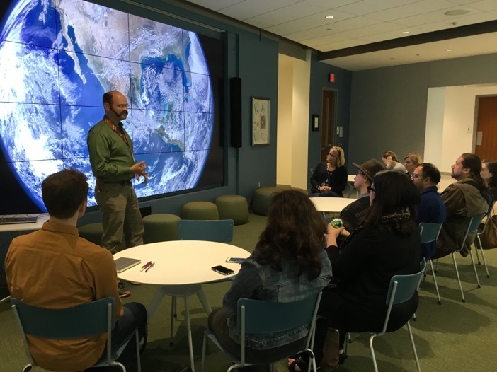 Global Studies IQ Wall with global map on screen with students listening to a professor in front.