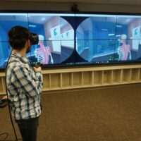 Ruth Lilly Medical Library IQ wall showing a double gaming screen with controlling VR headset on person in front.
