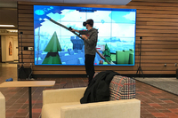 Whitewater Hall Lobby IQ wall with online gaming on screen with person wearing controlling VR headset in front.