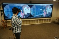Ruth Lilly Medical Library IQ wall showing a double gaming screen with controlling VR headset on person in front.